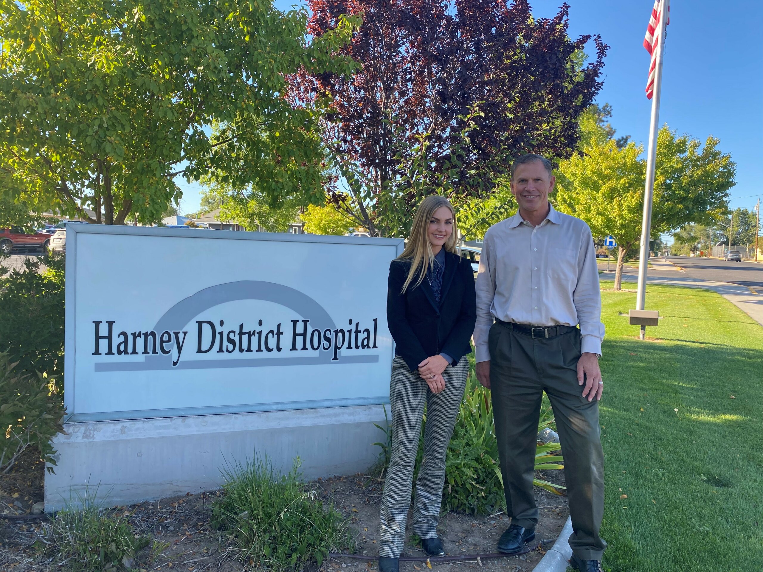 A photo of Sarah Lance and Dr. Moore standing next to the Harney District Hospital sign near the entrance of the hospital.
